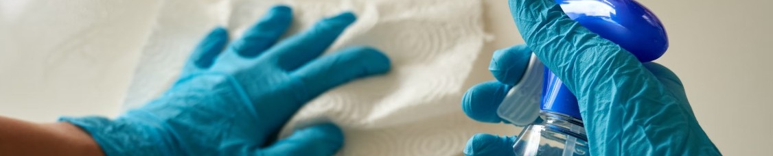 Person med blå handskar rengör yta med trasa och sprayflaska